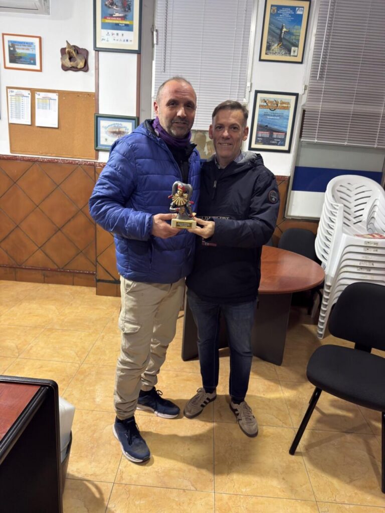 Carlos Javier Soler y otro hombre sosteniendo un trofeo en un evento de pesca.