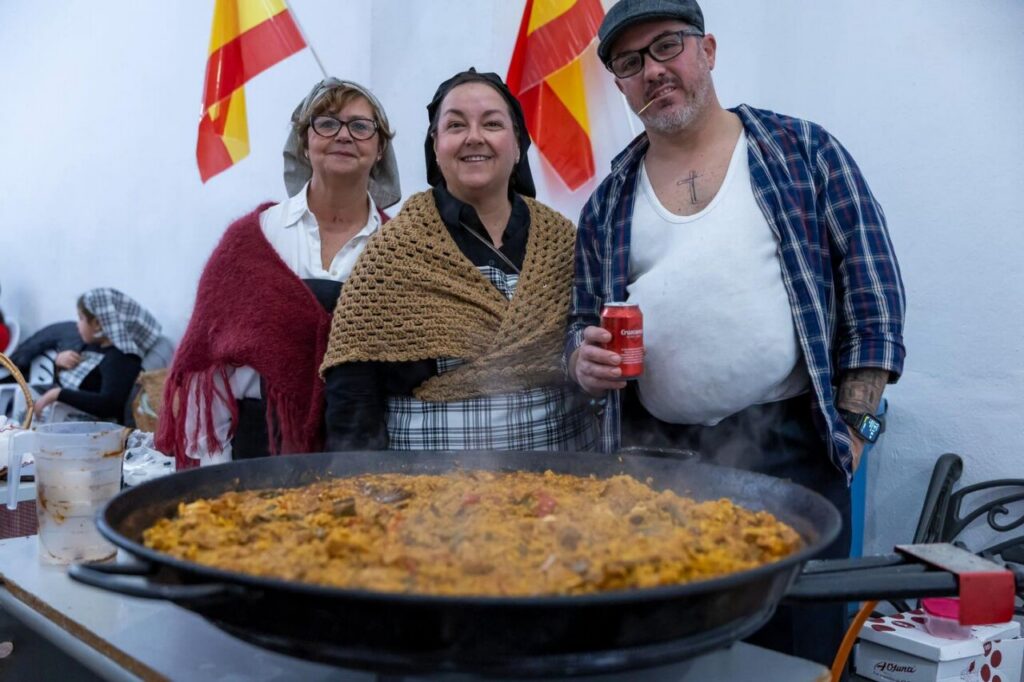 Tres personas sonrientes junto a una gran paella en el Carnaval de Melilla