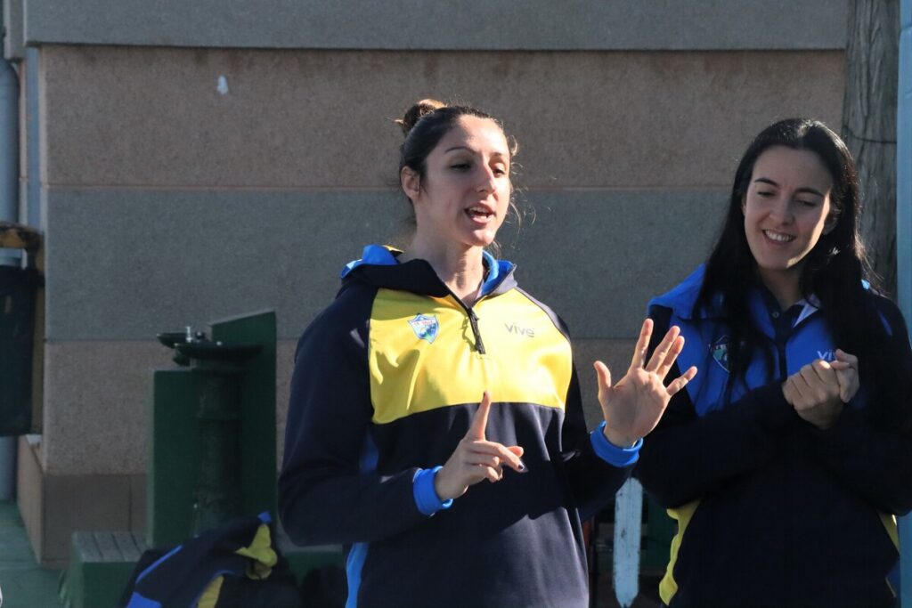 Dos entrenadoras conversando en un evento deportivo al aire libre