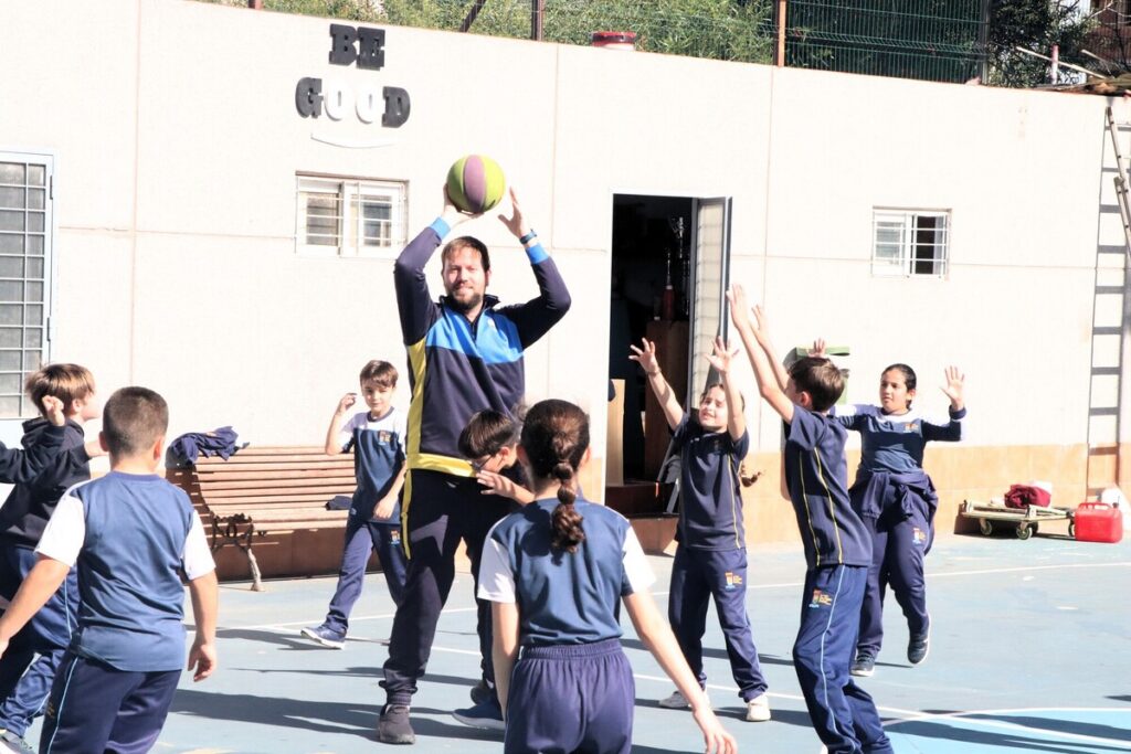 Niños jugando baloncesto en el patio de la escuela con un profesor.