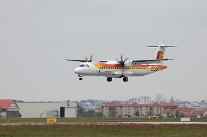 Avión aterrizando en un aeropuerto con edificios de fondo