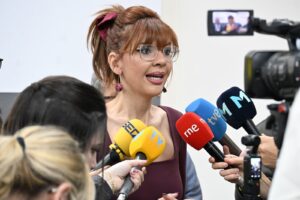 Mujer hablando a la prensa rodeada de micrófonos de diferentes medios