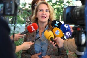 Mujer hablando a la prensa rodeada de micrófonos de diferentes medios.