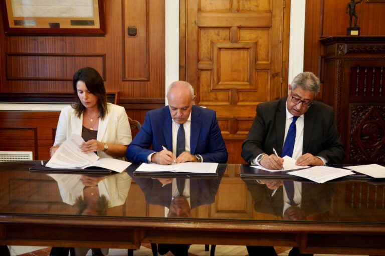 Tres personas firmando un convenio en una mesa de madera