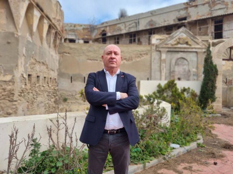 Hombre de pie frente a ruinas con jardín en primer plano.