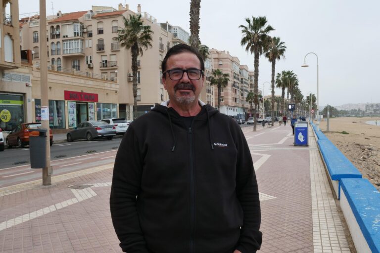 Hombre de pie en un paseo marítimo con palmeras y edificios