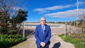 Hombre de pie frente a una playa con cielo azul y nubes.