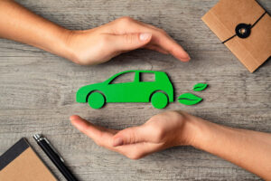 Manos protegiendo un coche verde sobre una mesa de madera