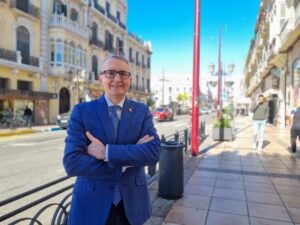 Hombre sonriente en traje azul en una calle con edificios