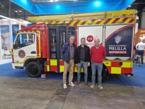 Tres personas posando junto a un camión de bomberos en Melilla