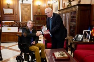 Enrique Mariñas entrega un libro al presidente de Melilla en su oficina.