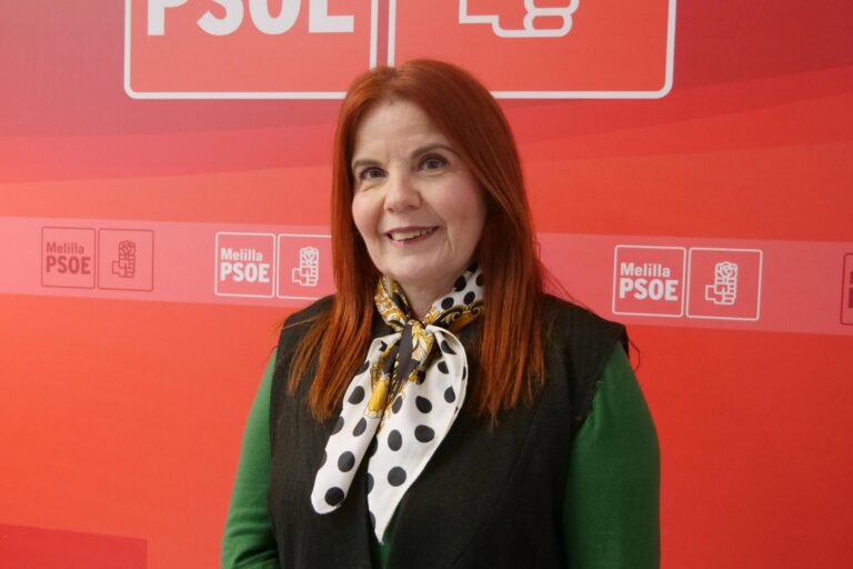 Retrato de mujer con cabello rojo y bufanda de lunares frente a fondo rojo.