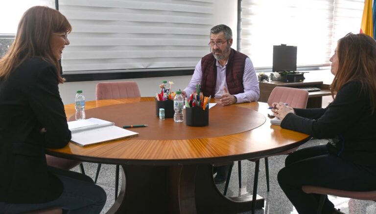 Tres personas sentadas en una mesa redonda durante una reunión en la oficina.