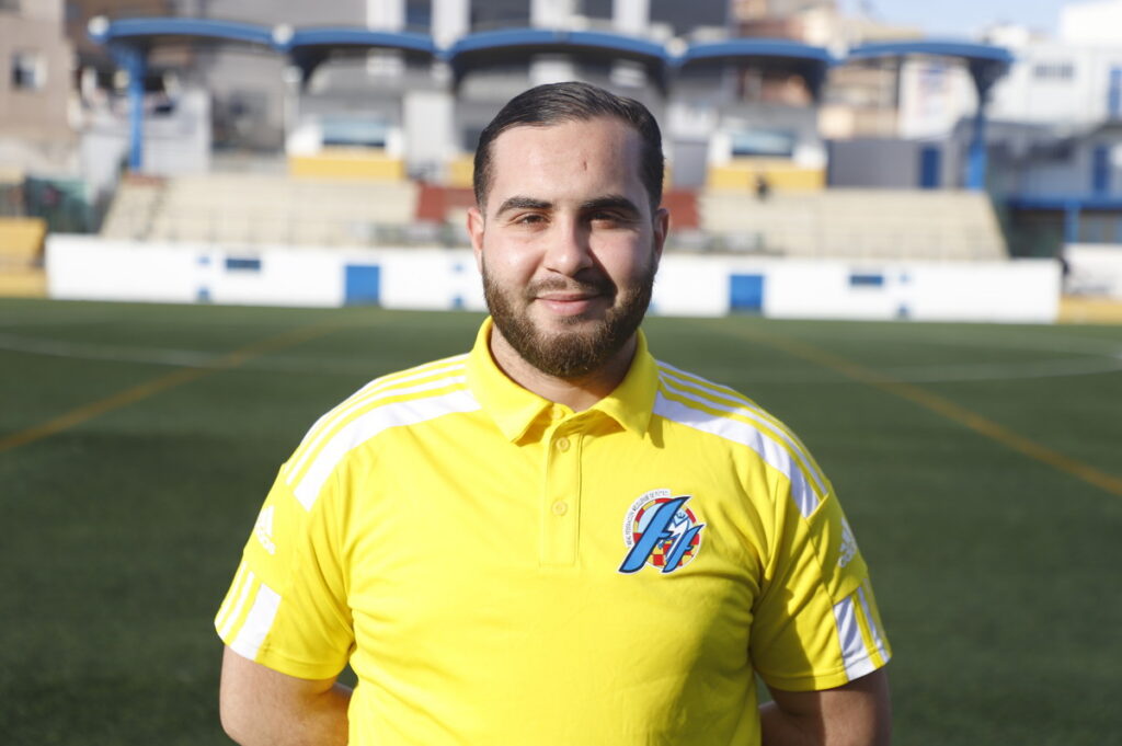Entrenador de fútbol con camiseta amarilla en un campo deportivo