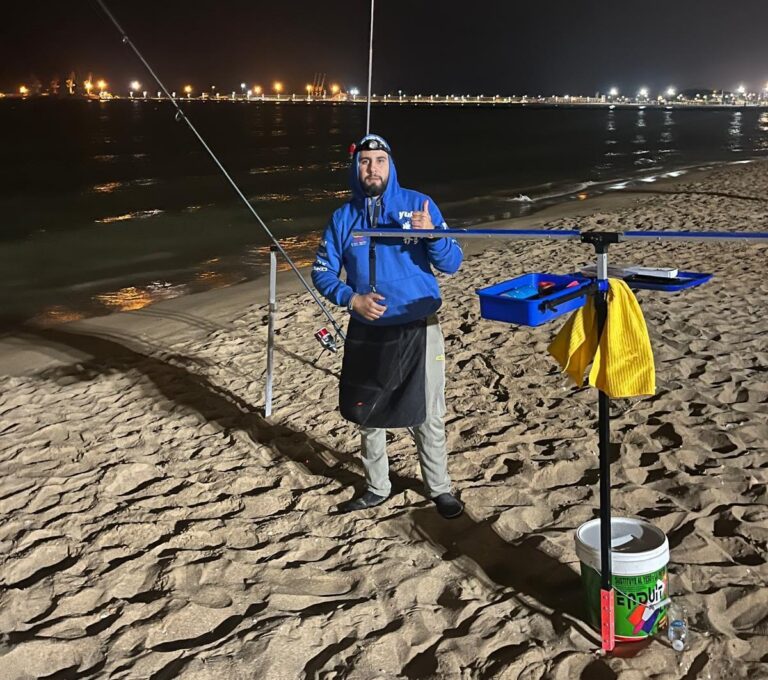 Hombre pescador en la playa durante la noche con caña de pescar