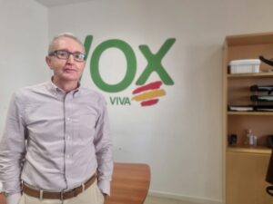 Hombre de pie en una oficina con el logo de VOX en la pared