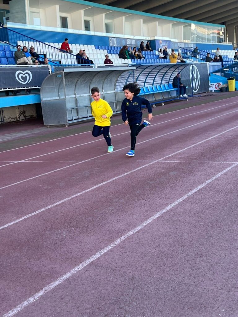 Dos jóvenes atletas corriendo en una pista de atletismo durante una competición.