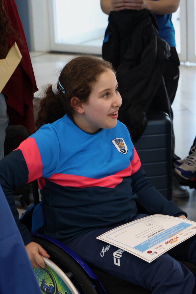 Niña sonriente en silla de ruedas con certificado en mano