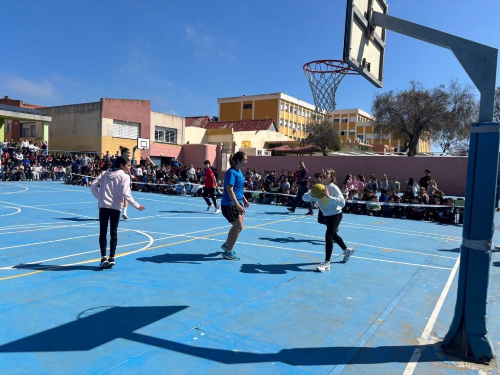 Jugadores de baloncesto interactuando con alumnos en el patio escolar.