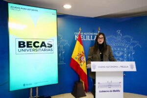 Presentación de becas universitarias en Melilla con una mujer en el podio.