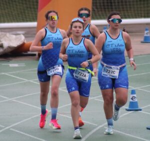 Cuatro mujeres corriendo en una competición de triatlón con uniformes azules.