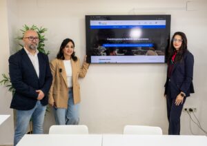 Tres personas posando frente a una pantalla con un mensaje sobre Melilla.