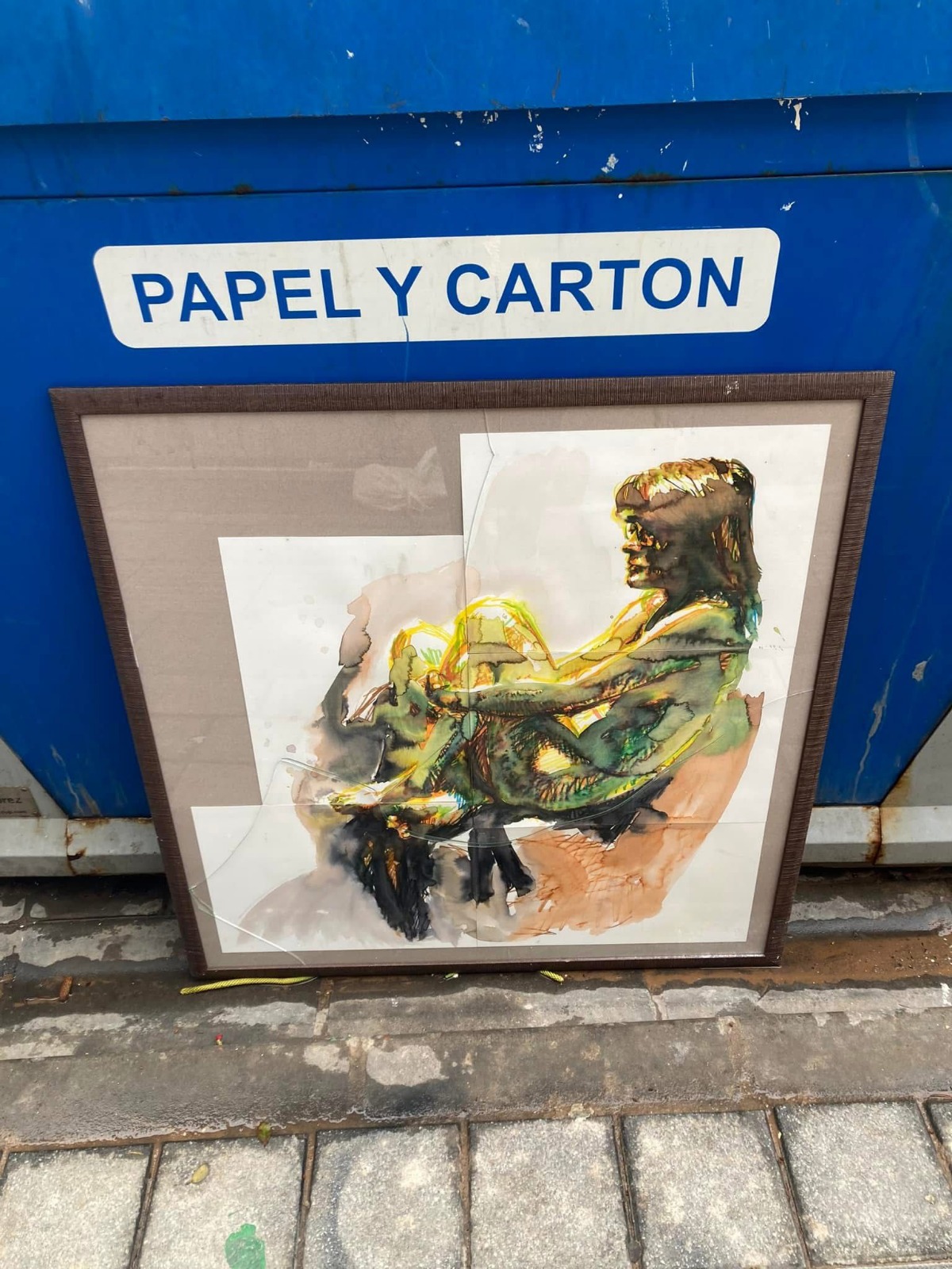 Cuadro roto apoyado en un contenedor de reciclaje azul
