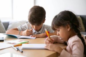 Niños estudiando en una mesa con cuadernos y lápices