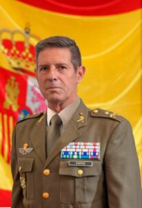 Retrato de un general en uniforme militar español con fondo de bandera.