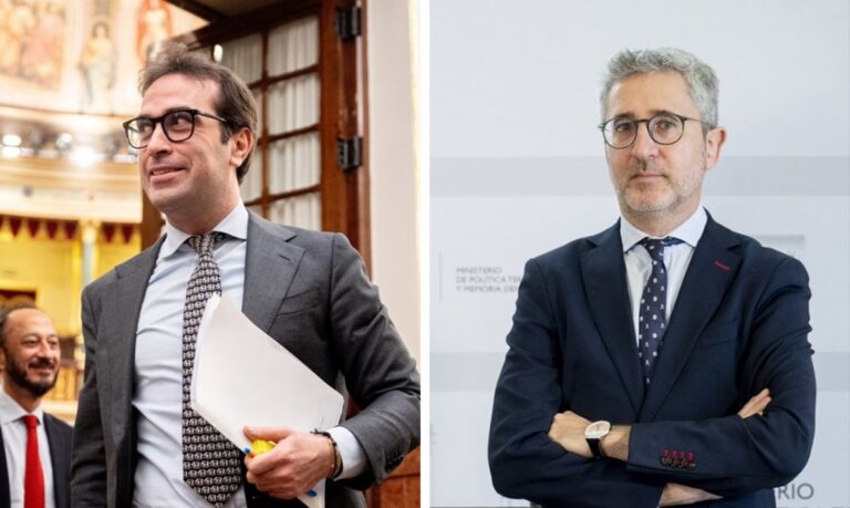 Dos hombres en una reunión política, uno sonriente y el otro serio.