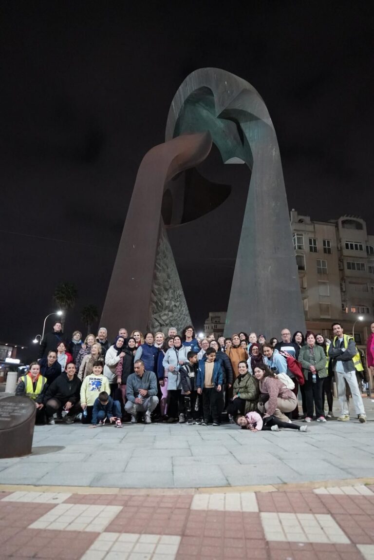 Grupo de personas posando frente a una escultura en la noche.
