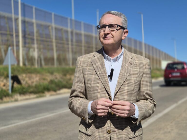 Hombre de pie frente a una valla en Melilla, con cielo azul.