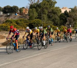 Grupo de ciclistas compitiendo en una carretera durante el Trofeo Melilla Ciudad del Deporte