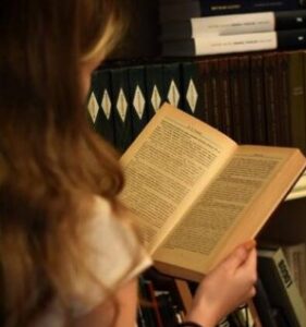 Joven leyendo un libro en una estantería de libros