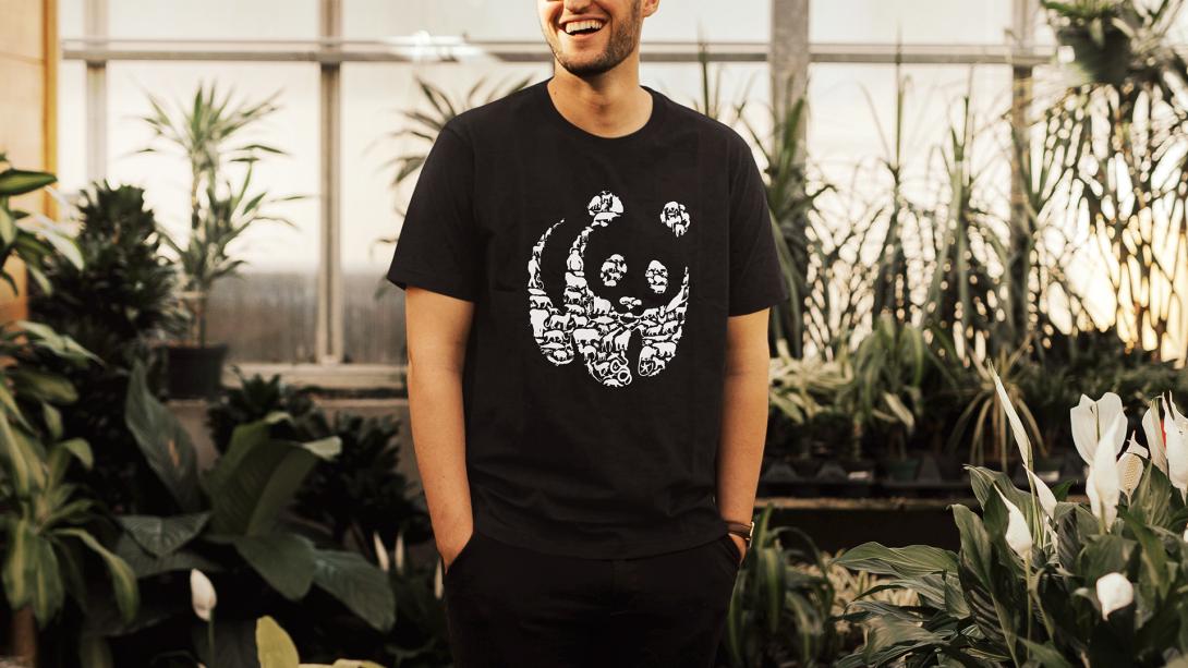 Hombre sonriente usando camiseta de La Hora del Planeta 2026 entre plantas