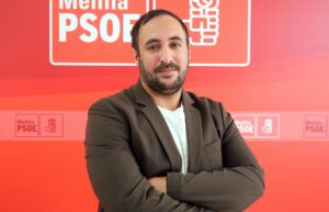 Persona de pie con brazos cruzados frente a un fondo rojo del PSOE en Melilla.