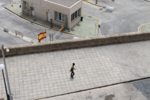 Un menor caminando en Melilla cerca de un edificio y una bandera española.