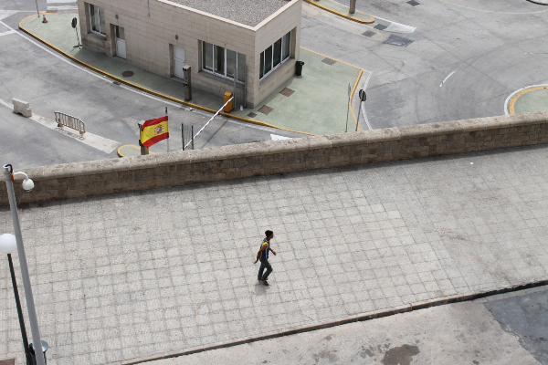 Un menor caminando en Melilla cerca de un edificio y una bandera española.