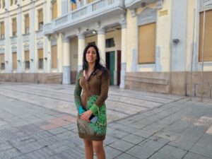 Mujer de pie frente a un edificio en Melilla con vestido colorido.