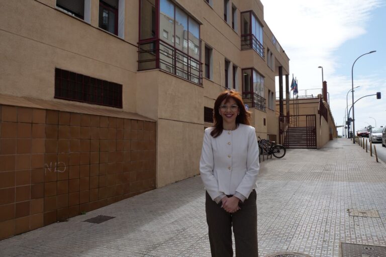 Mujer con cabello castaño y chaqueta blanca sonríe frente a un edificio.