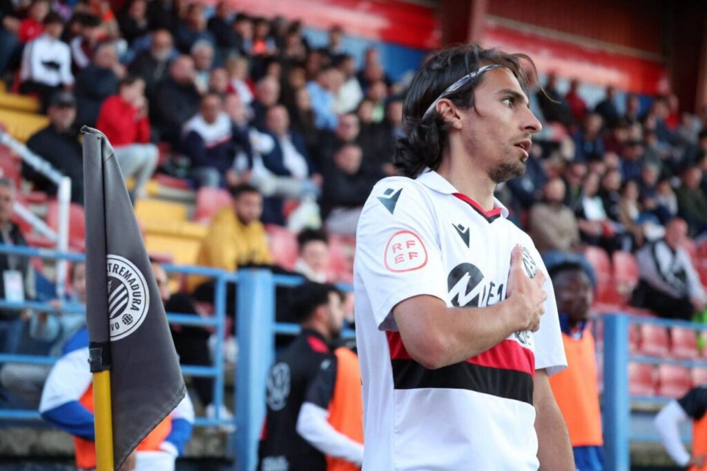 Jugador del C.D. Extremadura en un partido de fútbol con aficionados al fondo