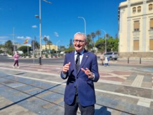 Hombre sonriente en traje en una calle soleada con edificios y palmeras
