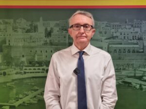 Retrato de un hombre con camisa blanca y corbata frente a un fondo histórico.