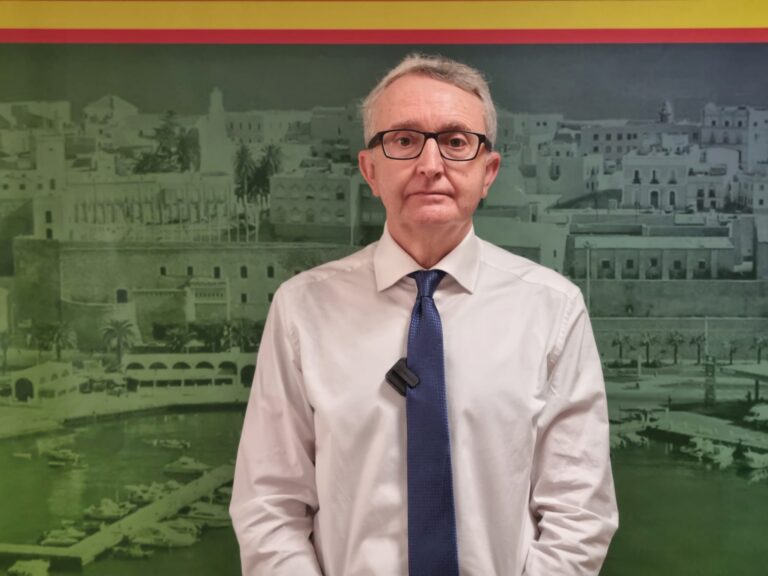 Retrato de un hombre con camisa blanca y corbata frente a un fondo histórico.