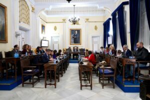 Reunión del consejo municipal en Melilla con miembros sentados en mesas.