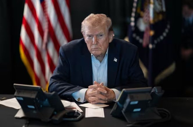 Donald Trump sentado frente a dos teléfonos en una mesa