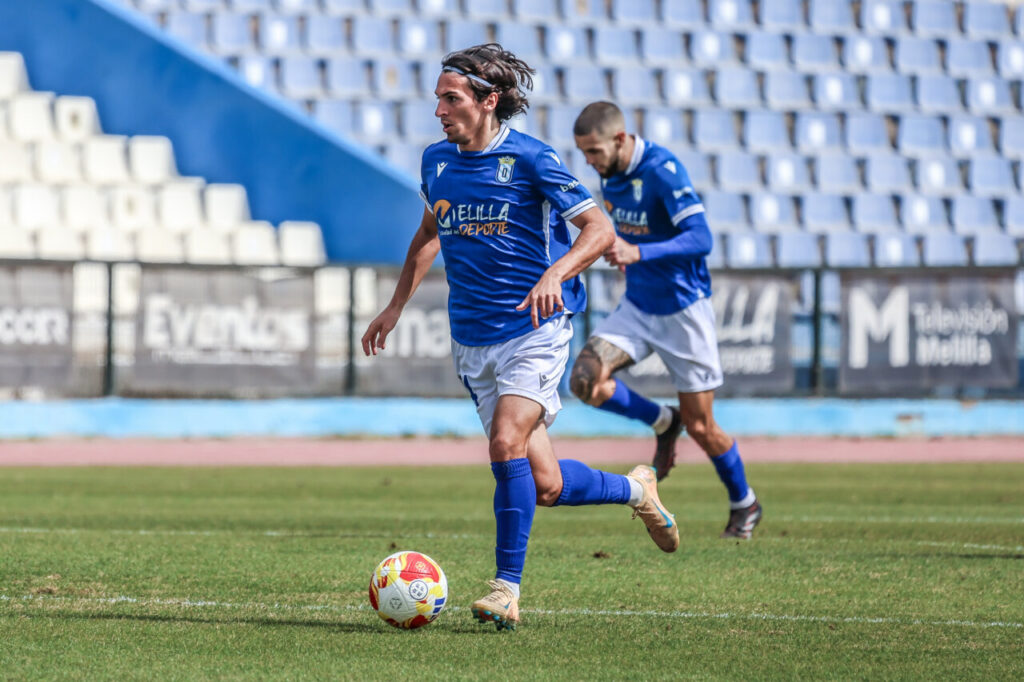 Jugador de la U.D. Melilla corriendo con el balón en un partido de fútbol