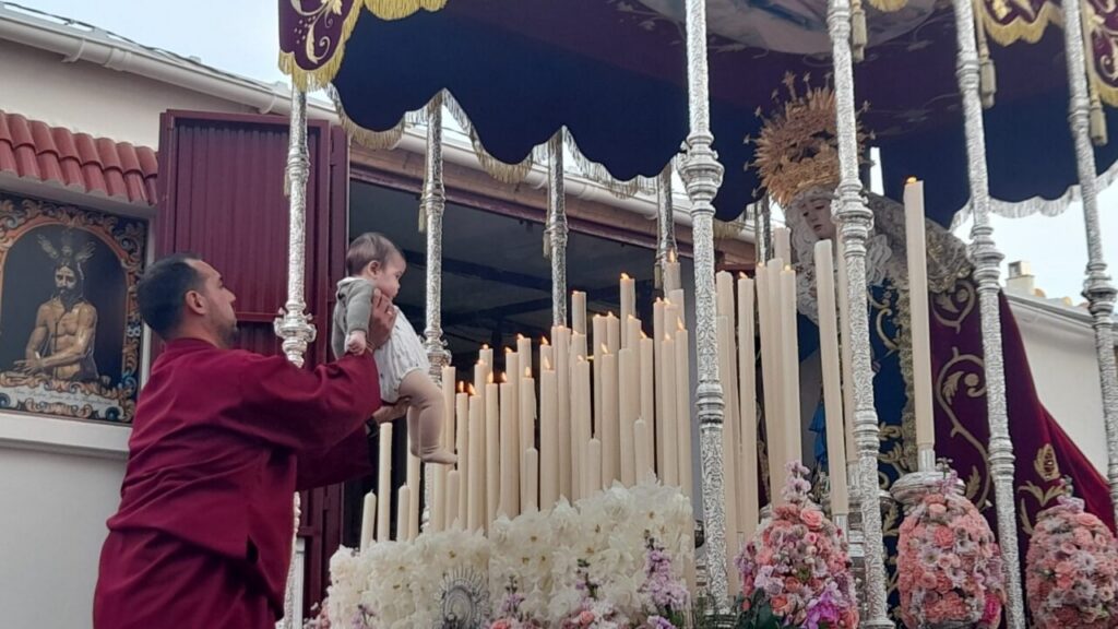 Hombre sosteniendo a un niño frente a una procesión religiosa en Melilla
