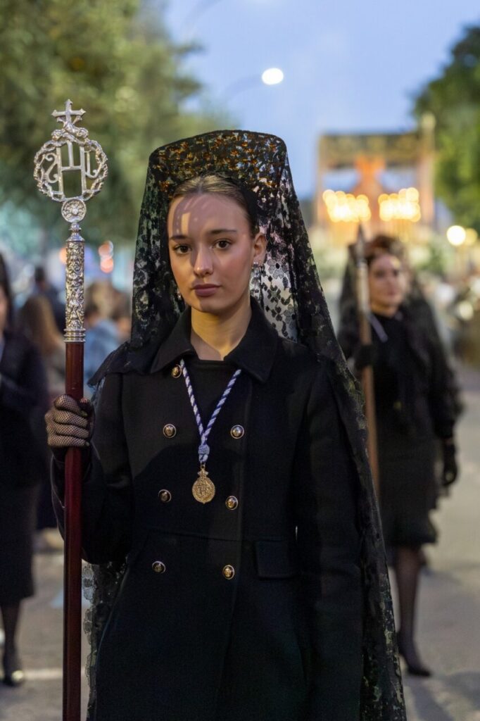 Joven cofrade con hábito negro y vara en procesión de Semana Santa