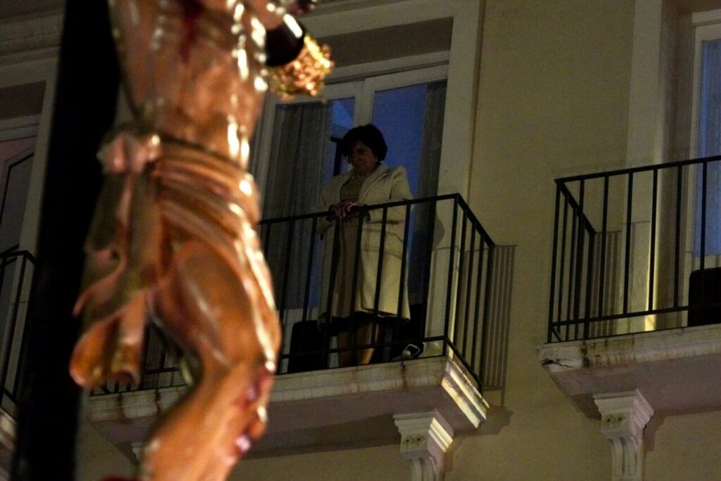 Mujer observando desde un balcón durante la procesión del Santísimo Cristo de la Paz en Melilla.
